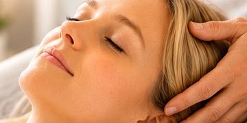 An adult resting with eyes closed, hands held gently at the crown of her head